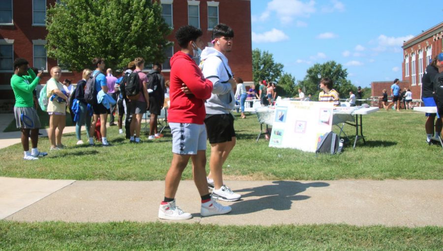 Two students walk past the interest fair, with a prominent crowd seen around the First Gen table.